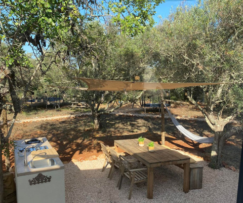 Buiten glampingruimte bij Algarve Olive Tree Lodge met houten tafel, hangmat en keuken tussen olijfbomen.