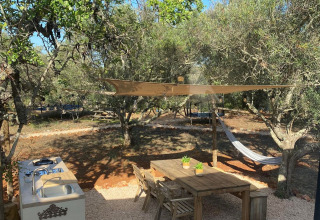 Area glamping all'aperto presso Algarve Olive Tree Lodge con tavolo in legno, amaca e cucina tra gli ulivi.