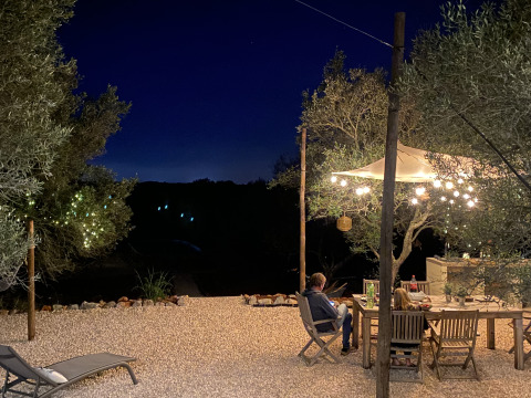 Outdoor dining area under fairy lights and trees at night at Algarve Olive Tree Lodge glamping site.