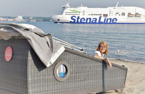 Donna si gode il glamping in una capanna sulla spiaggia nel fiordo di Kiel, traghetto Stena Line sullo sfondo.