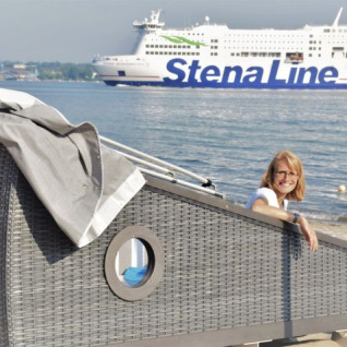 Mujer disfruta de glamping en una cabaña de playa en Kieler Fjord, con ferry de Stena Line al fondo.