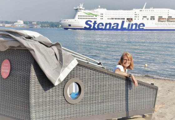 Femme profitant du glamping dans une cabane de plage au Kieler Fjord, ferry Stena Line en arrière-plan.