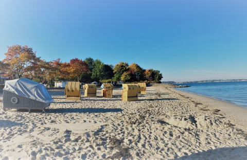 Strandmand-glamping aan het Kieler Fjord, op het strand met uitzicht op zee en kleurrijke herfstbomen.