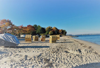 Beachside glamping in a Strandkorb at Kieler Fjord with ocean views and colorful autumn trees nearby.
