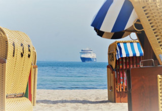 Uitzicht vanaf het strand in Kieler Fjord met strandstoelen en een cruiseschip in de verte, glampingstijl.