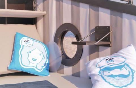 Alojamiento glamping con cojines náuticos, ojo de buey y estante en Kiel Sailing City, Kieler Fjord.