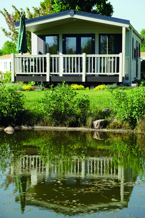 Chalet de glamping de luxe près d’un étang au Camping Südsee-Camp, entouré de verdure et nature.