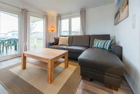 Moderne zithoek in luxe chalet op Camping Südsee-Camp, met grijze hoekzetel en houten salontafel.