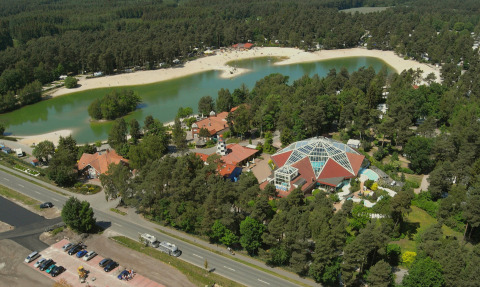 Vista aérea del Camping Südsee-Camp con lago, playa de arena, chalets de lujo y bosque en Baja Sajonia.