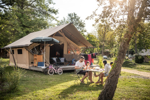 Familie isst zusammen vor einem Luxus-Zelt auf Camping Huttopia Lac de l'Uby - Glamping Occitanie.