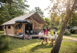 Familie nyder måltid foran et luksustelt på Camping Huttopia Lac de l'Uby - Glamping Occitanie.