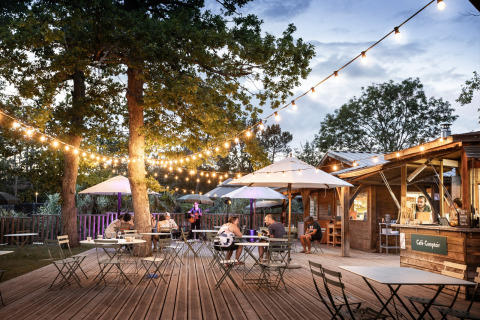 Gezellig buitenterras met lichtjes en parasols bij Camping Huttopia Lac de l'Uby - Glamping Occitanie.