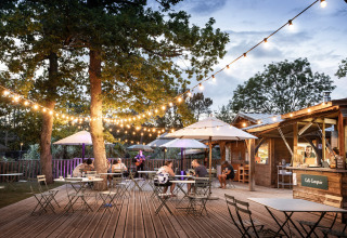 Buitenterras met sfeerverlichting en parasols bij Camping Huttopia Lac de l'Uby - Glamping Occitanie.