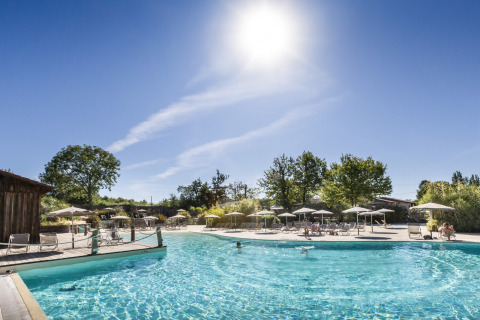 Piscina esterna con lettini e ombrelloni a Camping Huttopia Lac de l'Uby, Glamping Occitanie, in una giornata soleggiata.
