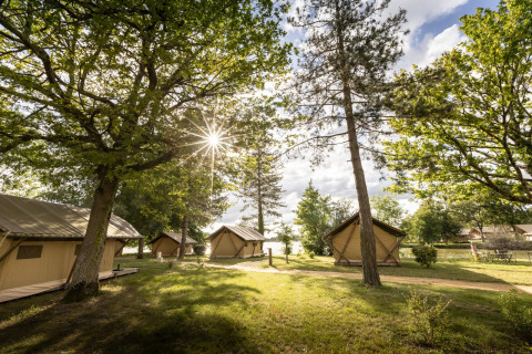 Tende glamping tra gli alberi al Camping Huttopia Lac de l'Uby in Occitania, splendente giorno di sole.