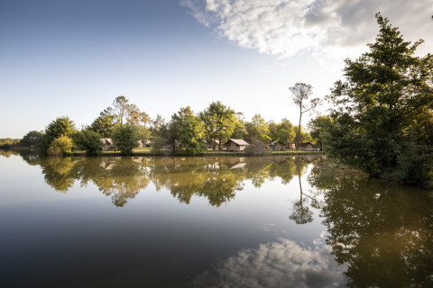 Glamping accommodaties bij Camping Huttopia Lac de l'Uby in Occitanie, weerspiegeld in een rustige vijver.