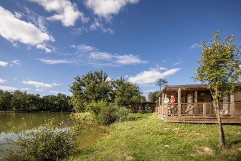 Wooden cabins by the lake at Camping Huttopia Lac de l'Uby - Glamping Occitanie under a blue sky.