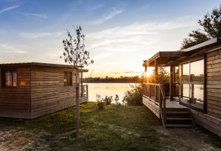 Houten chalets bij het meer tijdens zonsondergang op Camping Huttopia Lac de l'Uby - Glamping Occitanie, Frankrijk.
