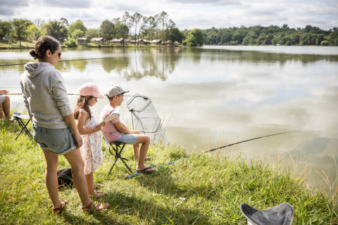 Familie fisker på søbredden ved Camping Huttopia Lac de l'Uby - Glamping Occitanie under solskinsvejr.