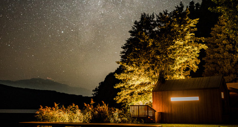 Glamping Unterkunft Biwak onder de Sterren in Österreich, beleuchtete Hütte am See unter sternenklarem Himmel.