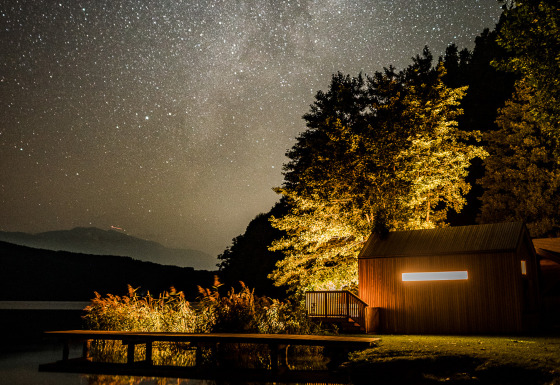 Alloggio glamping Biwak onder de Sterren in Austria, cabina illuminata sul lago sotto un cielo stellato.
