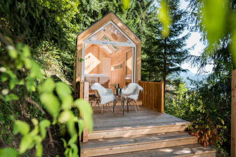 Luksuriøs glampinghytte i træ ved skoven med udendørs terrasse, møbler og naturskøn udsigt.