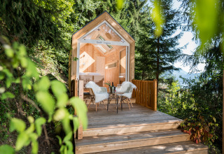 Cabaña de glamping de lujo en el bosque con terraza de madera, asientos cómodos y vistas a la naturaleza.