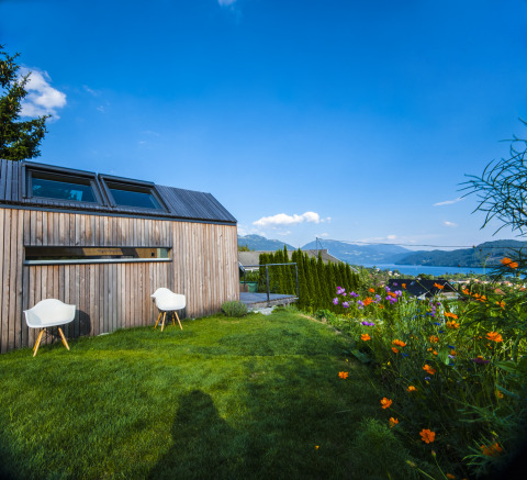 Glampingverblijf van hout met stoelen, bloemen en uitzicht op meer en bergen in Oostenrijk.