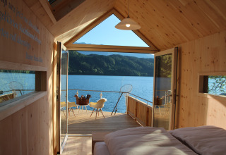 Luxe glampinghut met houten interieur, open deuren naar terras aan het meer en zicht op de bergen.