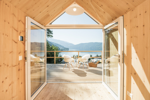 Alojamiento glamping de lujo con interior de madera, puertas abiertas y vistas al lago y montañas en Austria.