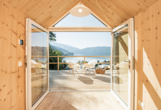 Alojamiento glamping de lujo con interior de madera, puertas abiertas y vistas al lago y montañas en Austria.
