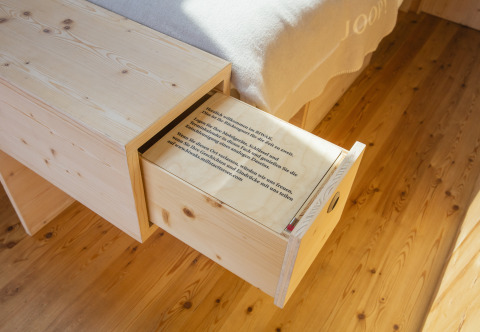 Tiroir en bois dans un lodge de glamping Biwak onder de Sterren, Autriche, plancher et lit visibles.