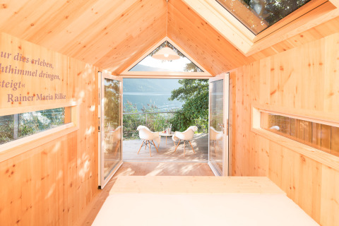 Interior de madera clara en glamping biwak con puertas abiertas a terraza y vistas a montaña y lago.