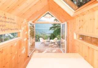 Licht houten interieur van glamping biwak met uitzicht op de bergen en het meer, deuren naar terras open.