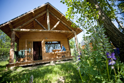 Cabane en bois à Huttopia Font-Romeu - Glamping Languedoc-Roussillon, entourée de verdure et de fleurs sauvages.