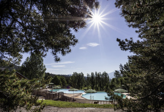Vista soleggiata sulla piscina di Huttopia Font-Romeu - Glamping Languedoc-Roussillon, circondata da alberi.