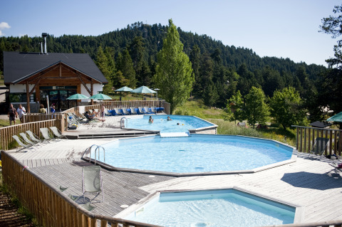 Outdoor pools and sun loungers at Huttopia Font-Romeu glamping site in Languedoc-Roussillon, surrounded by forest.