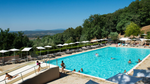 Large outdoor swimming pool with sun loungers and umbrellas at Vallicella Glamping Resort, Tuscany countryside view.