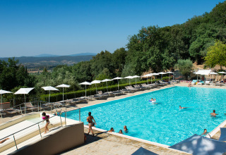 Großer Außenpool mit Sonnenliegen und Sonnenschirmen im Vallicella Glamping Resort in der toskanischen Landschaft.