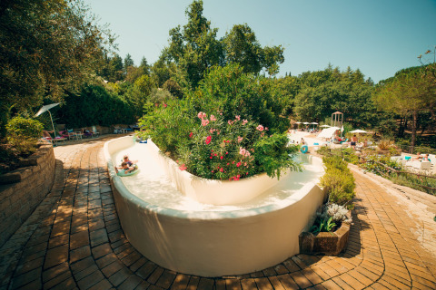 Outdoor water slide with lush greenery and flowering bushes at Vallicella Glamping Resort in Tuscany.