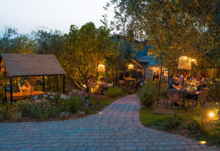 Zona de comedor al aire libre en Vallicella Glamping Resort, Toscana, con luces cálidas al atardecer.