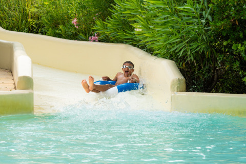 Kind rutscht lachend auf einer Wasserrutsche im Vallicella Glamping Resort, umgeben von grünen Pflanzen.