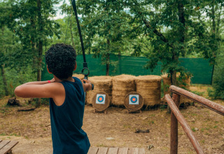 Niño haciendo tiro con arco en el bosque del Vallicella Glamping Resort, Cottages Toscane, Italia.