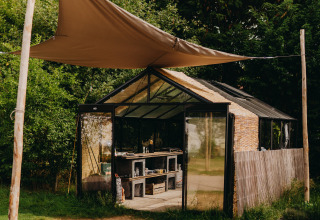 Alojamiento glamping en REBL Outdoor – Bell tenten Friesland, invernadero de cristal rodeado de vegetación.