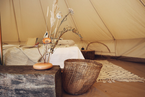 Binnenzicht van een glamping-tent bij REBL Outdoor Friesland met sfeervol bed, mand en houten decor.