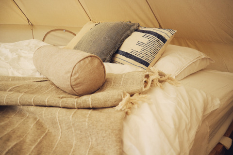 Cama de glamping acogedora en REBL Outdoor – Bell tents Friesland con almohadas suaves y manta cálida.