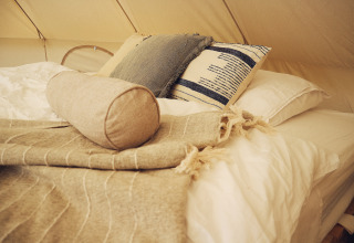 Gezellig glampingbed bij REBL Outdoor – Bell tenten Friesland met zachte kussens en een warme plaid.