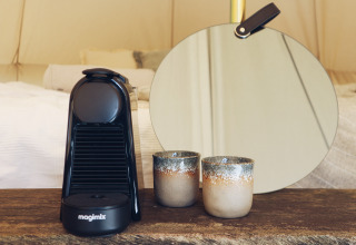 En kaffemaskine, to keramiske kopper og et rundt spejl på en træbord i REBL Outdoor Bell telte i Friesland.