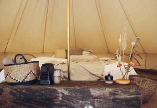Binnenzicht van een REBL Outdoor Bell tent in Friesland met een knus bed, manden en natuurdecoratie.