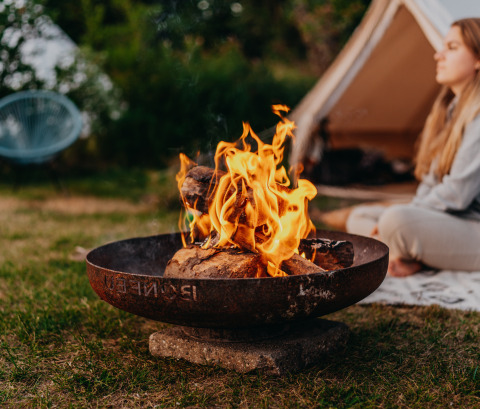 Bålplads foran et telt med en kvinde, der slapper af, hos REBL Outdoor – Bell tenten Friesland glamping.
